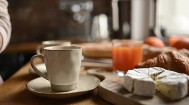 Kahvaltı için kahveye kruvasan ve peynirli krem peyniri koyan bir kız. Sabah yemeği hazırlamak için kapuçino espresso bardakları.