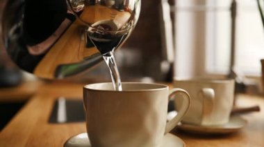 Mutfakta çay hazırlamak için çaydanlıktan sıcak su döken kişi. Çaydanlık ve seramik bardak ve sıcak içecek.