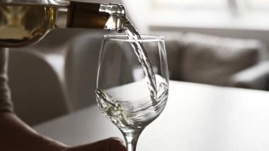 Adam yakın çekimde şişeden bardağa beyaz şarap dolduruyor. Şeffaf şarap kadehi ve şarap garsonu onu alkollü üzüm içeceğiyle dolduruyor.