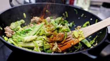 Meat with fresh vegetables cooking in asian wok pan. Red dry ground pepper is sprinkled on the food.