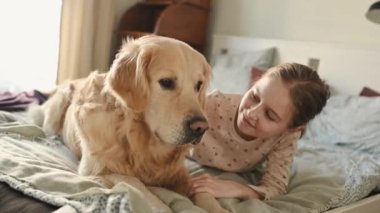Tatlı bir kız çocuğu Golden Retriever köpeğini okşuyor. Sabahları yatakta uzanıyor ve gülümsüyor. Safkan evcil köpek labrador 'u olan güzel çocuk uyandığında evde.