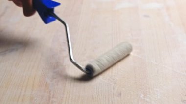 Zemin silindirli bir adam ahşap yüzeyi koruyucu beyaz renkle boyuyor. Ev dekorasyonu..