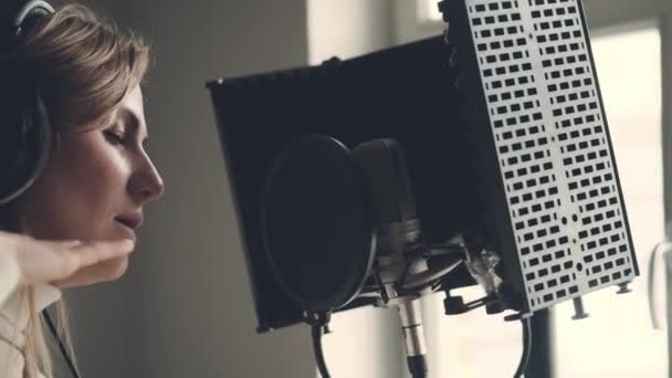 録音スタジオでヘッドフォンを装着したマイクで女の子の歌 歌の作成プロセス中に若い女性歌手の演奏室内 — ストック動画