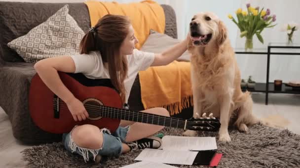 ギターを手にした少女10代の少女とペットと話す黄金のレトリバー犬をペット 楽器演奏中の女性の人間と純血犬は リビングルームでレッスンをプレイ — ストック動画