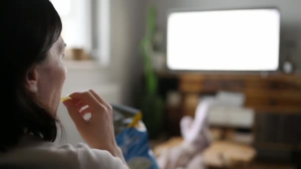 Γυναίκα Που Βλέπει Τηλεόραση Στο Σπίτι Και Τρώει Πατατάκια — Αρχείο Βίντεο