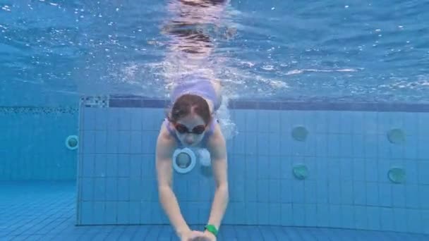 漂亮的少女带着戴眼镜的水泡在游泳池里游泳 漂泊在蓝水中的美女 — 图库视频影像