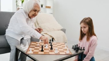 Küçük tatlı torunu olan büyük anne satranç oynuyor ve konuşuyor.