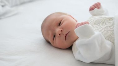 Beyaz kostüm giyen sevimli bebek portresi. Evde gün ışığında yatıp kameraya bakıyor. Masum güzel bebek yatak odasında dinleniyor.