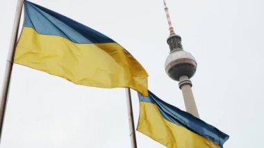 Ukrainian national flag waving on a flagpole against Berlin TV tower. Germany support Ukraine.