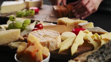 Roman peynirli brunost kesen bir kız. Peyniri üzümle, fıstıkla, peynir tabağıyla karıştır. Siyah arkaplanda şarap aperatifi.