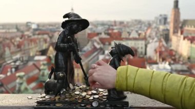 Tourist hand put coins to famous dwarf gnome sculpture in Wroclaw, Poland with city view. Money tradition and monument in Europe Union country