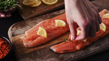 Ahşap tahtada limonlu taze somon filetosu pişirmeye hazırlanan bir kız. Taze pişmemiş kırmızı balık filetosu