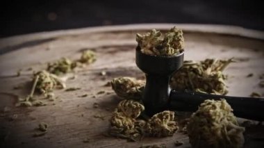 Kurumuş kenevir kenevir çiçekleri CBD açısından zengindir. Tahta bir tabakta sigara piposuyla döner, manzarayı kapatır.