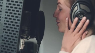 Girl singing with microphone wearing headphones in recording studio. Young woman pop singer perfomance