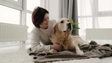 Golden retriever köpeği olan bir kız evde yerde uzanıyor, köpeğini okşuyor ve gülümsüyor, safkan evcil hayvanıyla birlikte genç bir kadın.