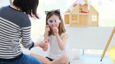 Anne ve tatlı küçük kız çocuk odasında oturmuş kağıt bardak ve dudaklarla oynuyorlar.