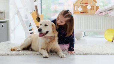 Mutlu küçük kız güzel oyun odasında sevimli köpeğe sarılıyor.
