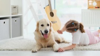 Tatlı Golden Retriever köpeği çocuk odasında yerde küçük bir kızı öpüyor.