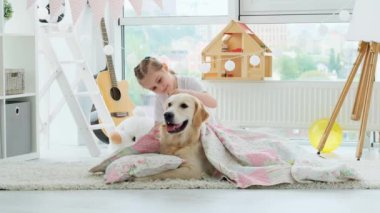 Güzel küçük kız, parlak odada güzel köpeğe battaniye örtüyor.