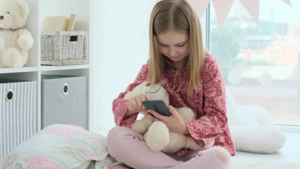 Menina Sorridente Brincando Com Smartphone Com Ursinho Pelúcia Sala Crianças — Vídeo de Stock