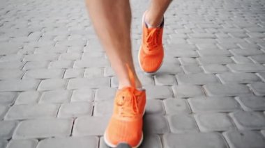Turuncu spor ayakkabılı bir adam şehir parkında asfalt yolda yürüyor.