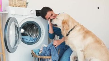 Woman with golden retriever dog playing while loading washing machine with clothes in light room