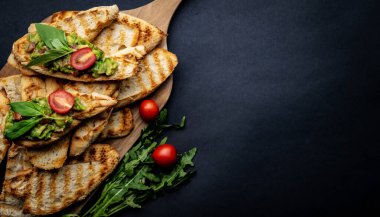 Tahta tahtada roka ile servis edilen tost, guacamole, fesleğen ve vişneli domates. Dilimlenmiş ekmek, avokado, otlar ve sebzelerle harika yemek kompozisyonu.