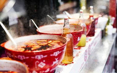 Beverages fruits and berries hot mulled wine in red pots in street food market. Colorful hot drinks at fair festival outdoors closeup