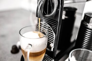 Kapsüllü kahve makinesi evdeki mutfakta şeffaf bardakta kapuçino hazırlıyor. Espresso kafein üreticisi ve kremalı İtalyan içeceği.