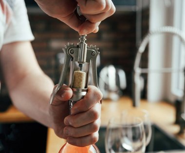 Man opening wine bottle and glasses on table at kitchen