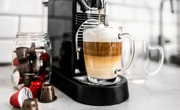 カプセルとクリーミーなカプチーノとコーヒーマシンは 自宅で透明なカップに エスプレッソカフェイン飲料メーカーとイタリアのドリンク — ストック写真