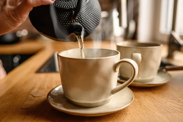 お茶を淹れるために台所で釜からお湯を注ぐ人 暖かい飲み物とティーポットとセラミックマグカップ — ストック写真