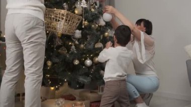 Mutlu aile süs balolarını evde Noel ağacına asıyor.