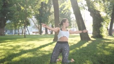 Genç kız çimenlerde yoga yapıyor ve sabahları doğayı dengede tutuyor. Yazın dışarıda egzersiz yapan bir kadın.