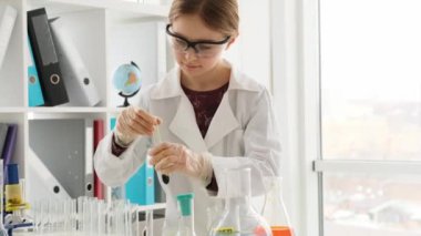 Korunma gözlüğü takan liseli kız kimya sınıfında tüpler ve sıvılarla çalışıyor. Laboratuvarda ekipmanla okuyan kız öğrenci.