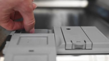 Girl put dishwasher pill and close the door of a dishwasher at kitchen. Woman and washer machine at home