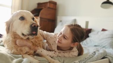 Tatlı bir kız çocuğu Golden Retriever köpeğini okşuyor. Sabahları yatakta uzanıyor ve gülümsüyor. Safkan evcil köpek labrador 'u olan güzel çocuk uyandığında evde.