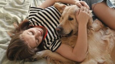 Güzel kız Golden Retriever köpeğini kucaklıyor yatakta yatıyor ve gülümsüyor, yukarıdan bakıyor. Güzel bayan, safkan evcil köpek labrador 'u evinde dinleniyor.