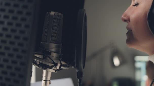 録音スタジオでヘッドフォンを装着したマイクで女の子の歌 歌の作成プロセス中に若い女性歌手のパフォーマンス — ストック動画