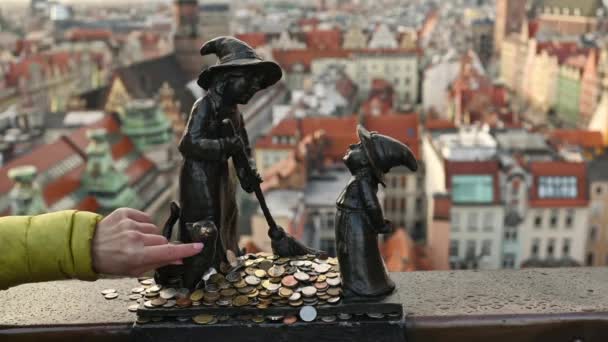 観光客の手はコインを入れ 街の景色を望むポーランドのヴロツワフで幸運のための有名なドワーフのノーム彫刻に触れます 欧州連合 の国のお金の伝統と記念碑 — ストック動画
