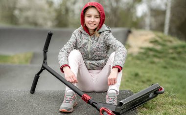 Cute little girl with a scooter in a extreme ride park, smilling and looking into the camera