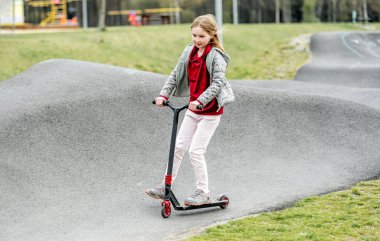 Beautiful little girl rides a scooter in a extreme ride park