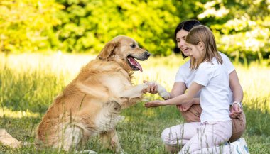 Anne ve tatlı kız dışarıda Golden Retriever köpeğiyle oynuyorlar.