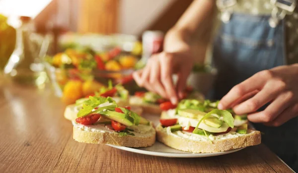 キッチンのクローズアップでアボカド トマト グリーンでサンドイッチを準備する少女の手 新鮮な野菜とアルグラを備えたベジタリアンブロシェッタス — ストック写真