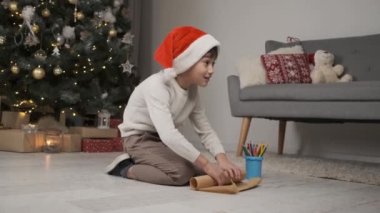 Kırmızı şapkalı küçük çocuk Noel Baba 'ya evde Noel ağacının altında otururken mektup yolluyor.