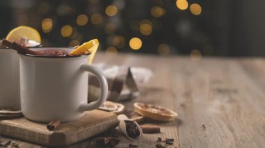 Çelik bardaklarda tarçın ve limonla süslenmiş sıcak şarap yılbaşı aydınlatma arka planında duruyor.