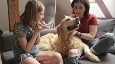 Güzel kız ve genç çocuk kanepede oturan Golden Retriever köpek kulaklarıyla konuşuyor. Safkan evcil köpekli bir anne ve kız.