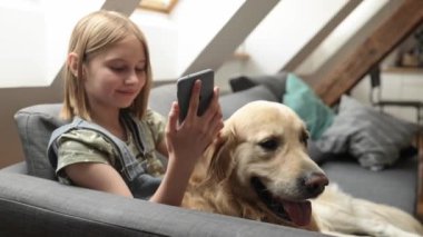 Golden Retriever köpeği olan kız akıllı telefonda sohbet ediyor. Cep telefonundan sosyal medyaya bakan safkan köpekli şirin bir çocuk.