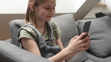 Akıllı telefonlu kız evdeki kanepede oturuyor sosyal medyadan arkadaşlarıyla sohbet ediyor ve gülümsüyor. Cep telefonuyla mesajlaşan güzel bir çocuk.
