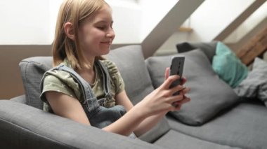 Akıllı telefonlu kız evdeki kanepede oturuyor sosyal medyadan arkadaşlarıyla sohbet ediyor ve gülümsüyor. Cep telefonuyla mesajlaşan güzel bir çocuk.